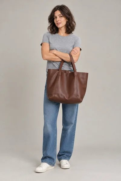 A mesma mulher de braços cruzados com uma bolsa grande marrom cobrindo a roupa