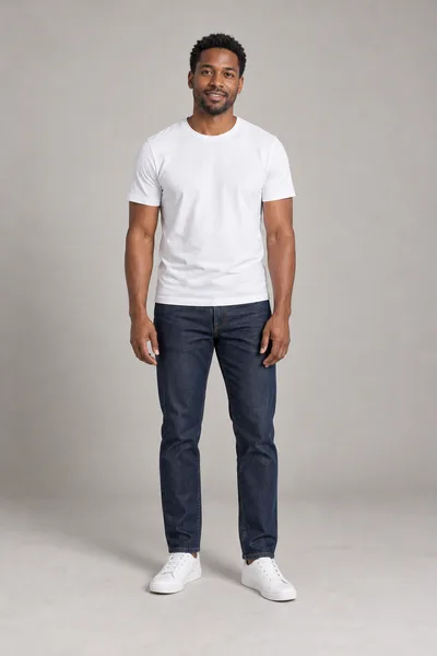 Homem de cabelo curto e barba rala, de camiseta branca, calça jeans escura e tênis branco, em pé num estúdio cinza-claro — prévia do trocador de roupa com IA
