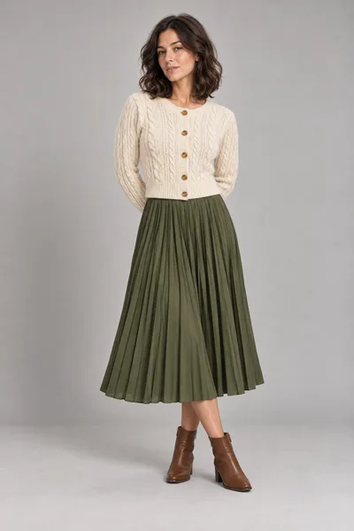 A mesma mulher com o cardigã creme, a saia plissada verde-oliva e as botas marrons do flat lay — prévia do trocador de roupa com IA