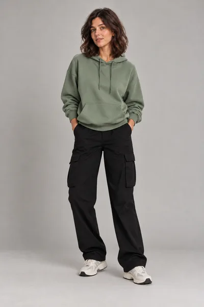 Mulher de moletom oversize verde-sálvia com capuz, calça cargo preta e tênis branco — prévia do trocador de roupa com IA