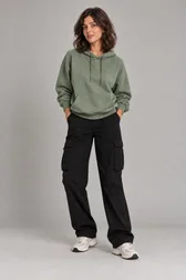 Mulher de moletom oversize verde-sálvia com capuz, calça cargo preta e tênis branco — prévia do trocador de roupa com IA